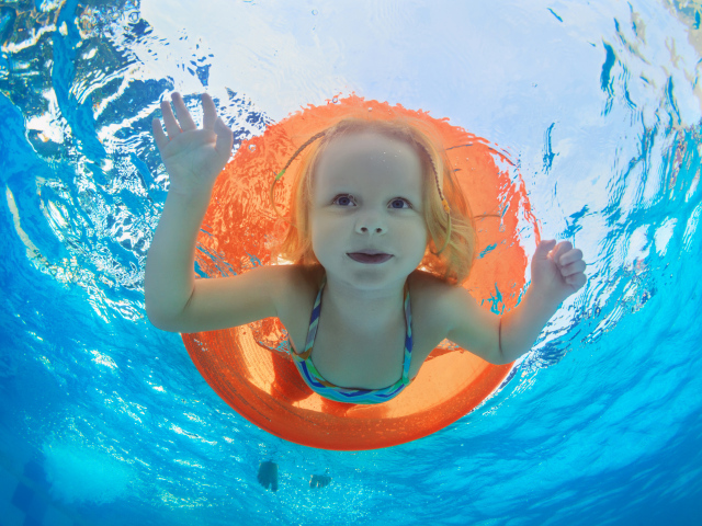 Маленькая девочка плавает в бассейне со спасательным кругом