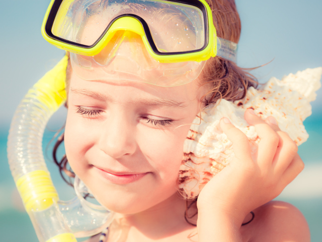 Маленькая девочка приложила ракушку к уху