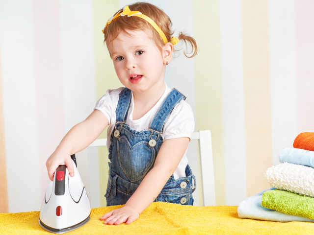 Маленькая девочка с утюгом гладит полотенце