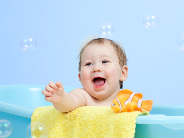 Веселый малыш купается в ванной с игрушечной рыбкой