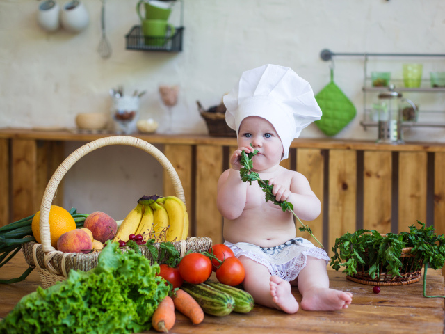 Маленький ребенок в шапке повара сидит на столе с овощами