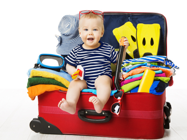 Маленький ребенок сидит в большом красном чемодане с вещами
