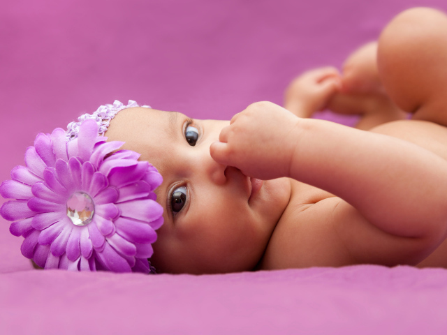 Младенец девочка с большим сиреневым цветком на голове 