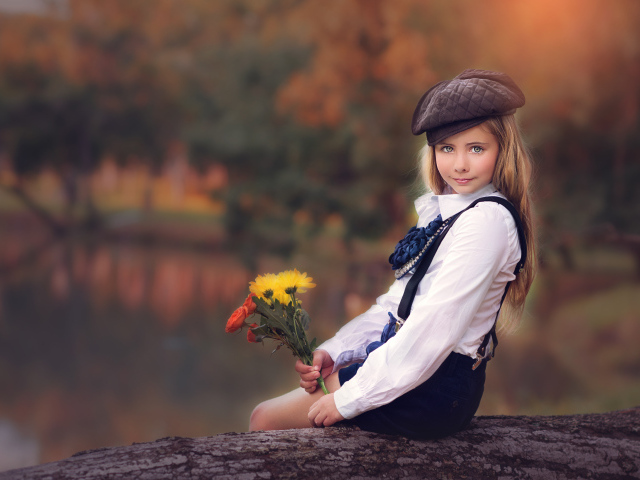 Красивая девочка в кепке с букетом в руках сидит на дереве
