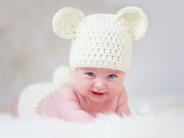 Голубоглазый грудной ребенок в белой вязаной шапке с ушками