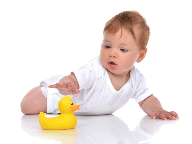 Грудной ребенок с желтой резиновой уточкой на белом фоне