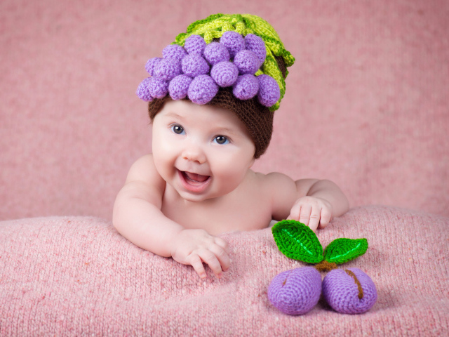 Забавный грудной ребенок в вязаной шапке с ягодами на голове