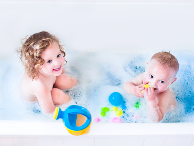 Маленькие мальчик и девочка купаются в ванной с игрушками