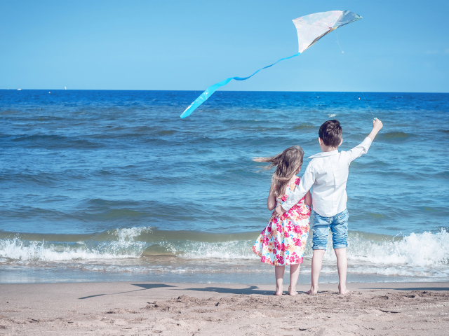 Маленькие мальчик и девочка запускаю воздушного змея на пляже