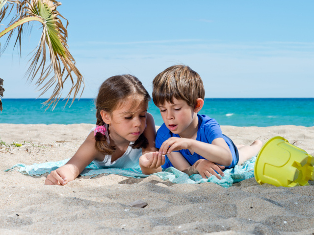 Маленькие мальчик и девочка играют на песке у моря