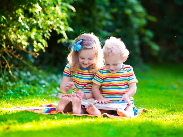 Маленькие мальчик и девочка читают книгу сидя на зеленой траве
