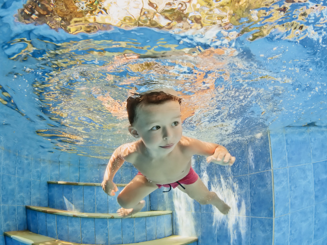Маленький мальчик плавает под водой в бассейне