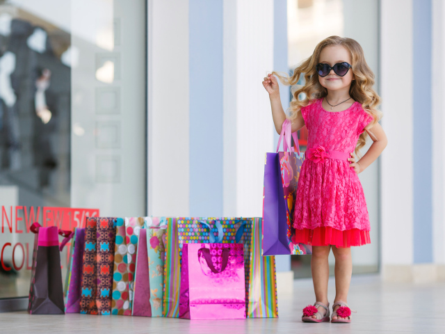 Маленькая модная девочка в красном платье с покупками
