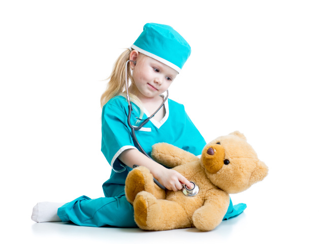 Маленькая девочка в костюме врача лечит плюшевого медвежонка