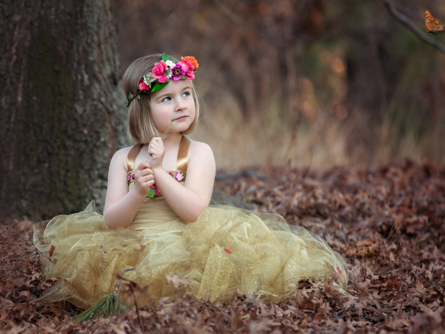 Маленькая девочка в красивом платье сидит на сухой листве