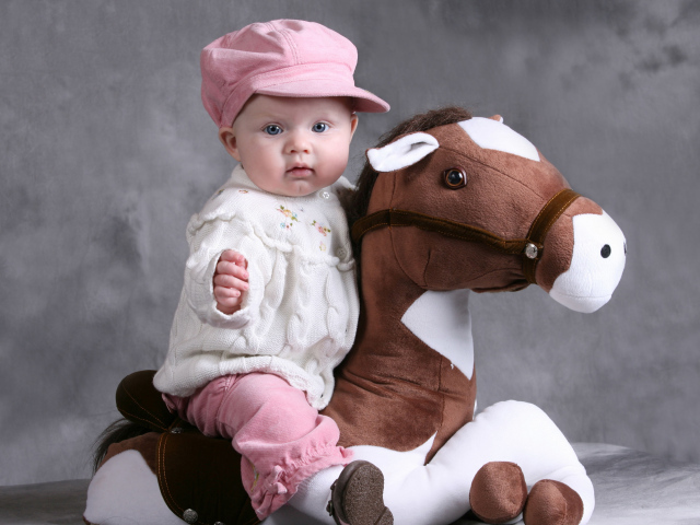 Маленькая девочка в розовой кепке сидит на игрушечной лошади
