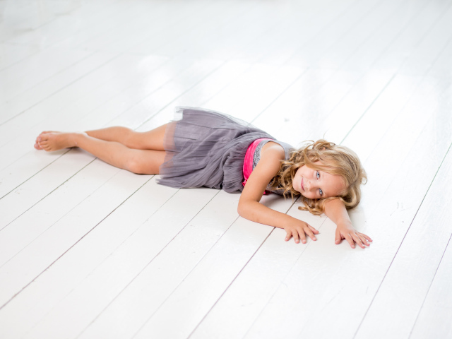 Маленькая девочка модель в сером платье лежит на деревянном полу