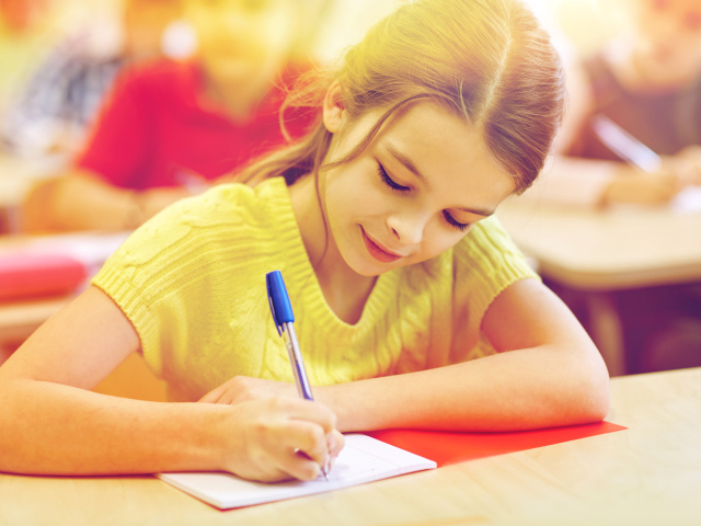 Маленькая девочка школьница пишет ручкой в тетради