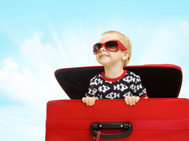 Маленький улыбающийся мальчик в очках сидит в красном чемодане