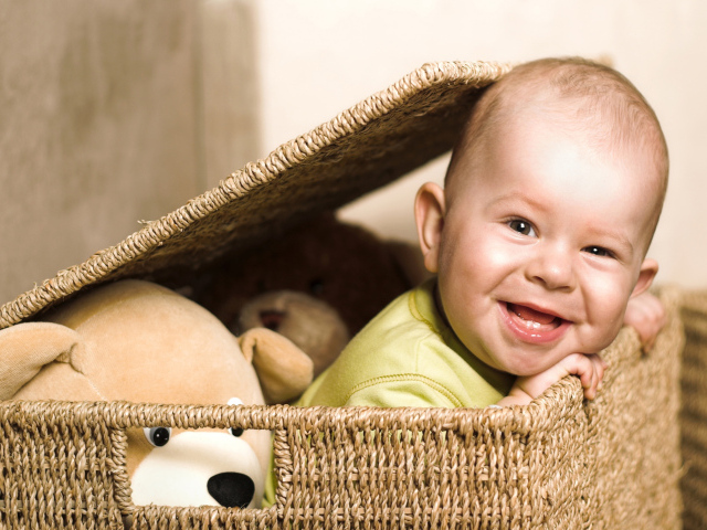 Маленький улыбающийся ребенок сидит в корзине с игрушками