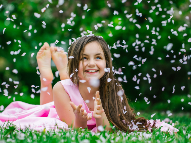 Маленькая улыбающаяся девочка шатенка ловит лепестки