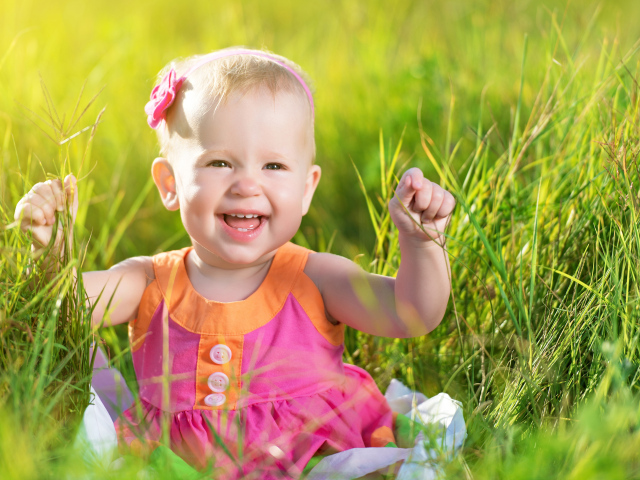 Маленькая улыбающаяся девочка сидит в зеленой траве
