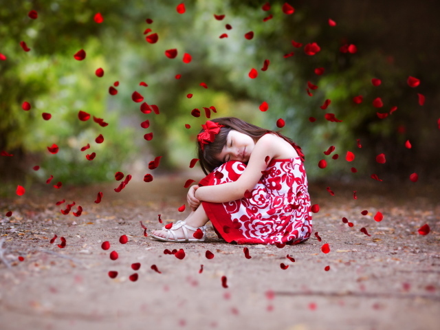 Лепестки красной розы падают на маленькую девочку