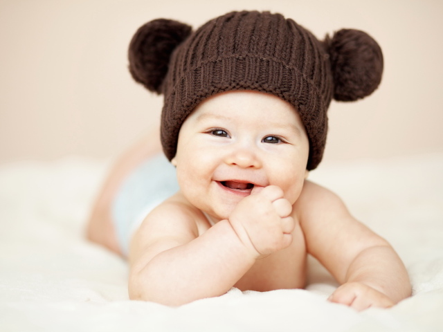 Улыбающийся грудной ребенок в коричневой вязаной шапке