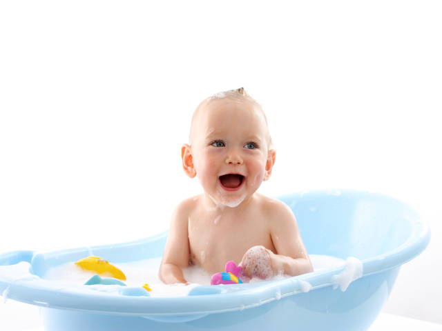 Улыбающийся грудной ребенок сидит в синей ванночке на белом фоне