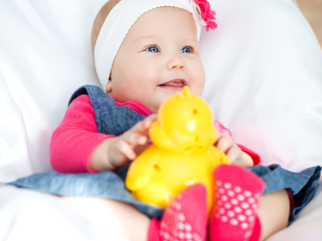 Улыбающаяся голубоглазая девочка младенец с игрушкой в руках