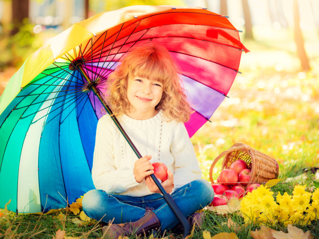 Улыбающаяся девочка с корзиной яблок сидит под разноцветным зонтом