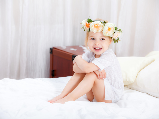 Улыбающаяся девочка с венком на голове сидит на кровати