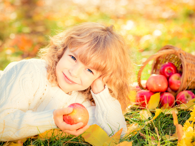Улыбающаяся рыжеволосая девочка с корзиной красных яблок