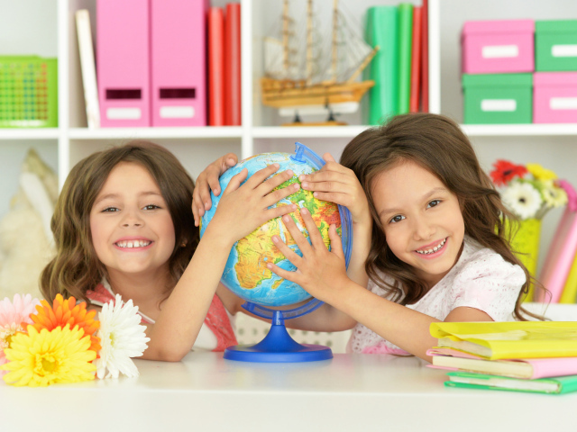Две маленькие девочки школьницы с глобусом  в руках
