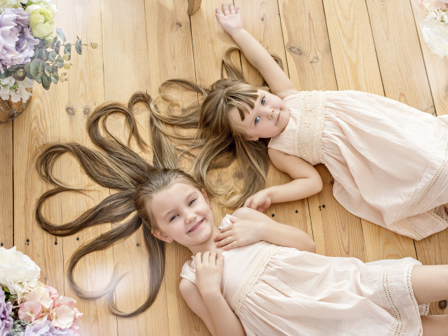 Две маленькие девочки с длинными волосами лежат на полу