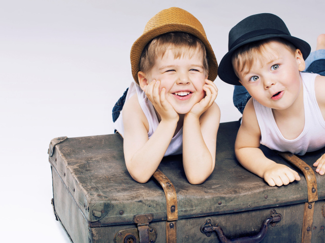 Два маленьких улыбающихся мальчика лежат на старом чемодане