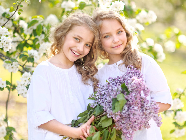 Две улыбающиеся девочки близняшки с букетом сирени