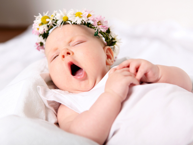 Зевающая маленькая девочка с венком из цветов на голове