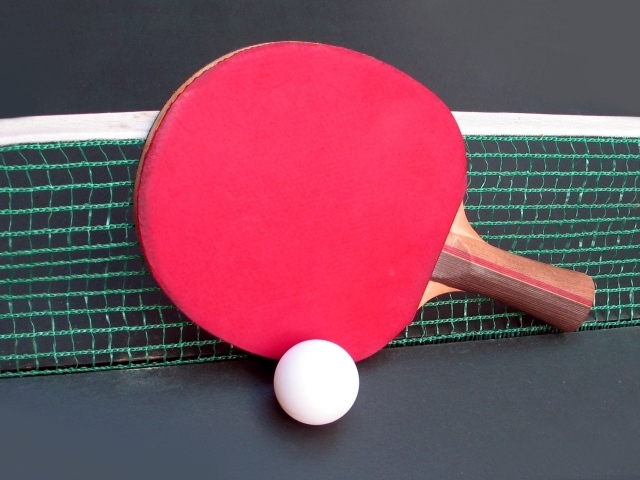 Красная ракетка для настольного тенниса у сетки 