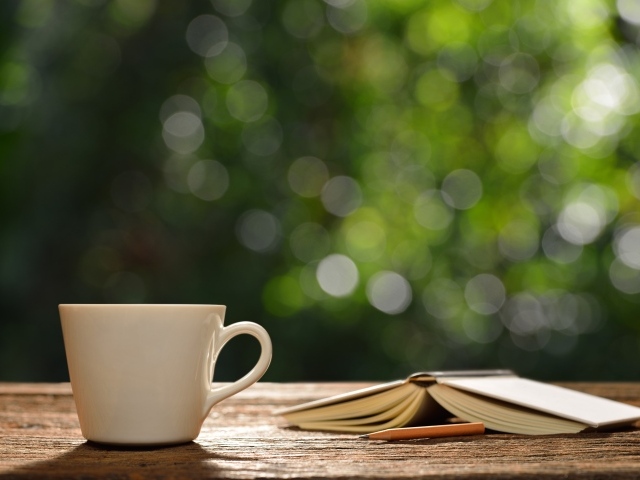 Белая чашка на столе с открытой книгой