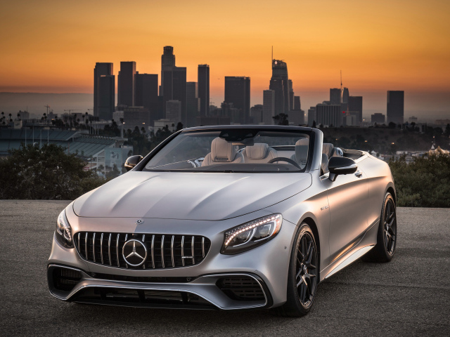 Серебристый автомобиль Mercedes AMG S63 4MATIC Cabriolet, 2018 на фоне мегаполиса