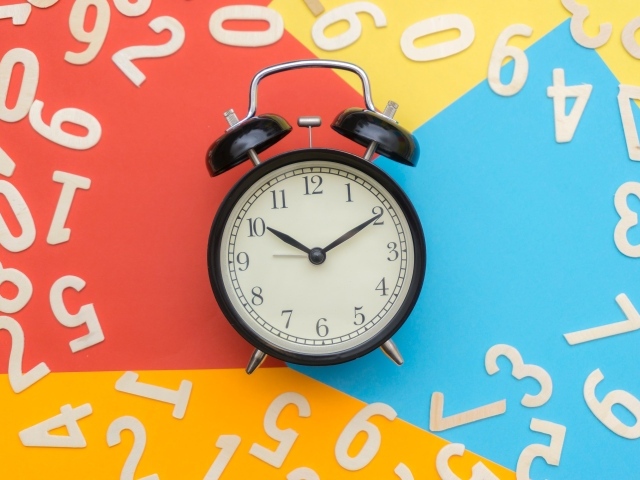 Будильник на разноцветном фоне с цифрами