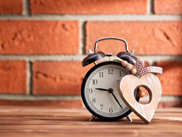 Будильник с деревянным сердцем стоит на фоне стены