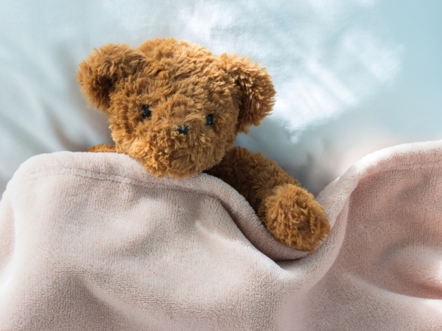 Плюшевый медведь в кровати под одеялом