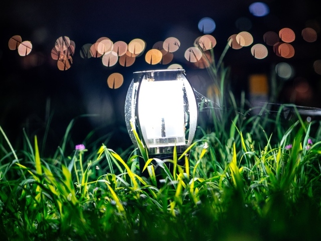 Включенный фонарь стоит в зеленой траве