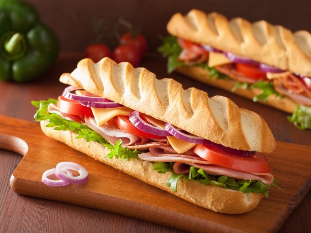 Аппетитный сэндвич с ветчиной, листьями салата, помидорами и луком