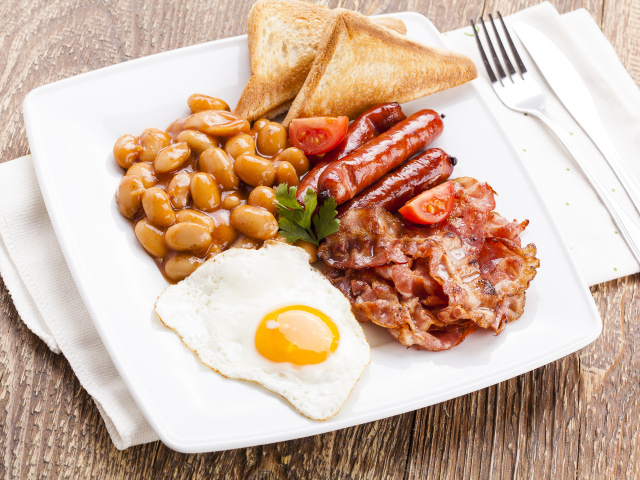 Бекон, яичница, фасоль и сосиски на тарелке к завтраку 