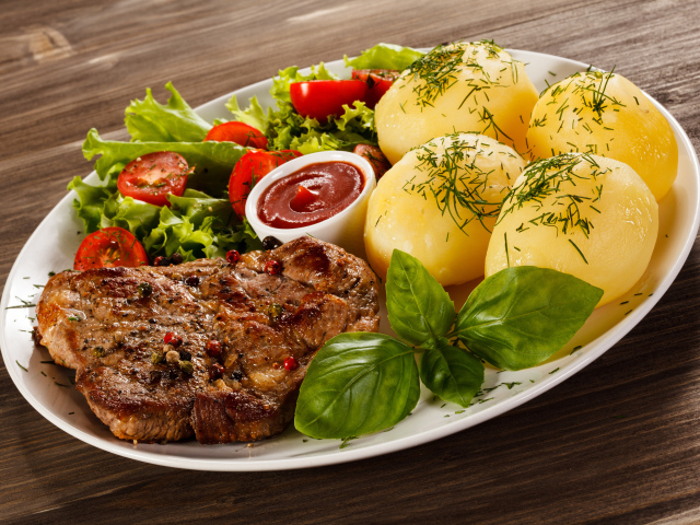 Вареный картофель с куском мяса и салатом на тарелке