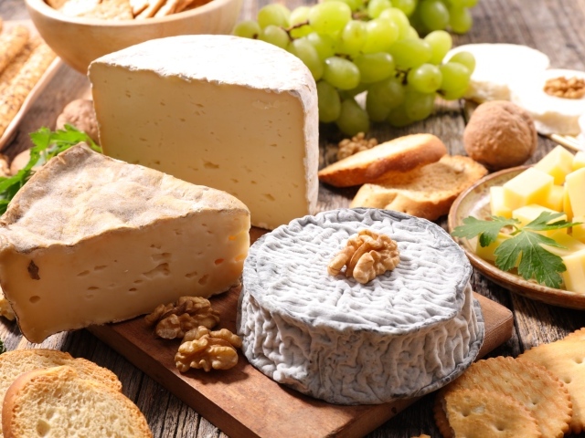 Сыр с плесенью на столе с виноградом, орехами и хлебом