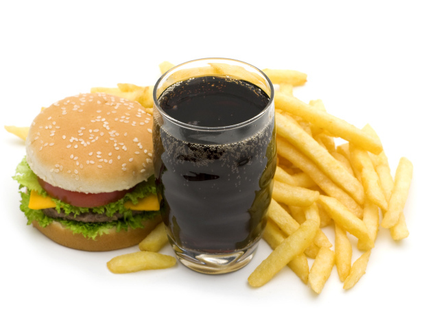 Кола в стакане на столе гамбургером и картофелем фри на белом фоне